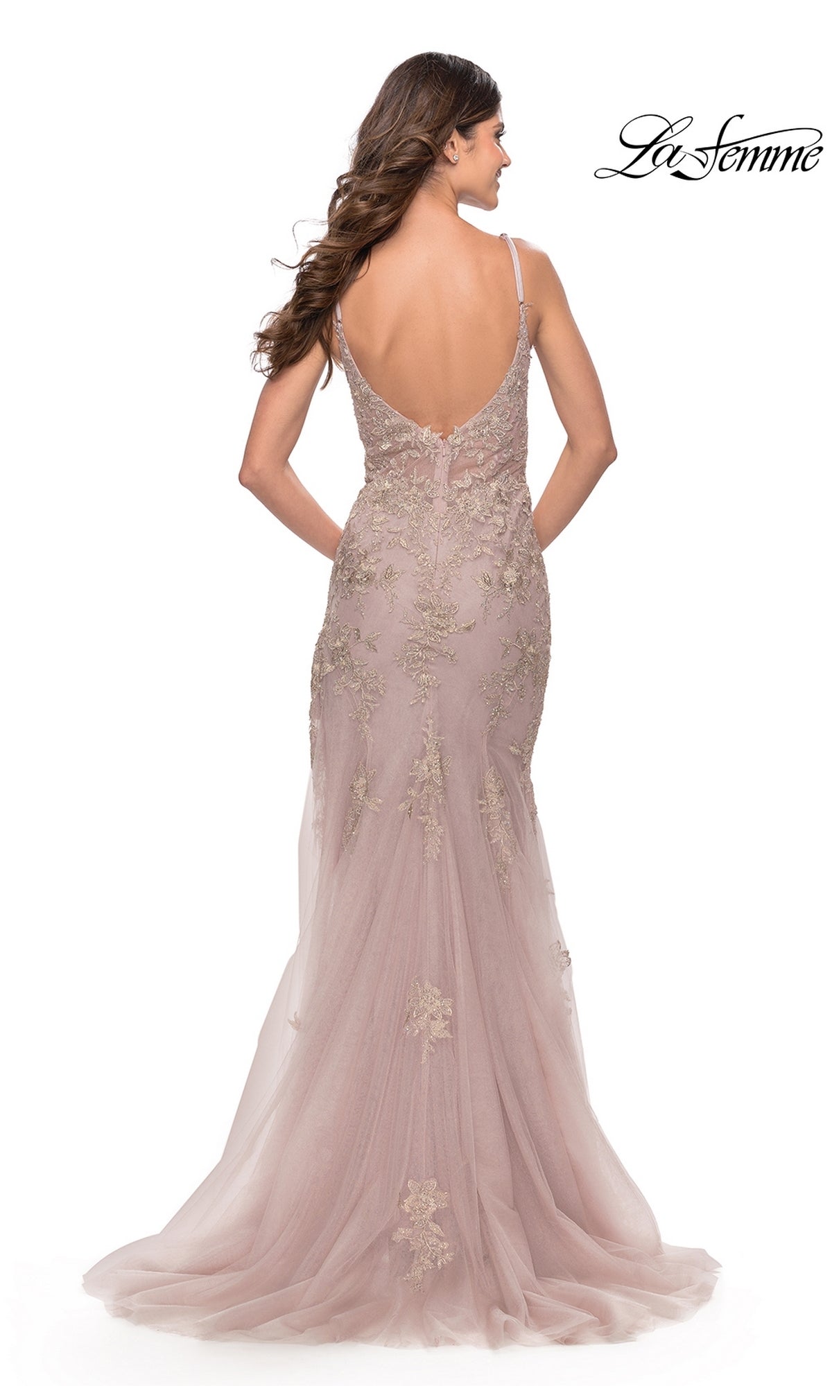 A woman models the La Femme Long Lace Prom Dress with a blush pink hue, gold embroidery, spaghetti straps, and a low back against a white background.